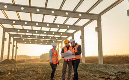 Three construction workers stood under a structure with plans
